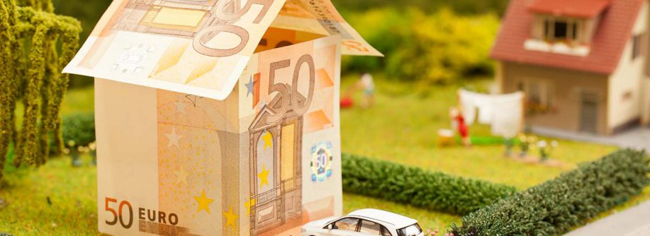 Modellhaus aus 50 Euro Scheinen in einem Garten mit einem weißen Spielzeugauto vor der Tür | Immobilienfinanzierung