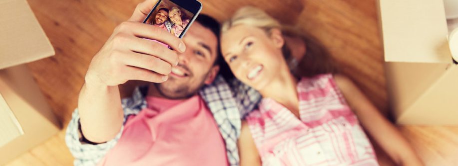 Ein junges Paar liegt glücklich auf dem Fußboden in seiner neu gekauften Immobilie und macht ein Selfie | Immobilienkauf