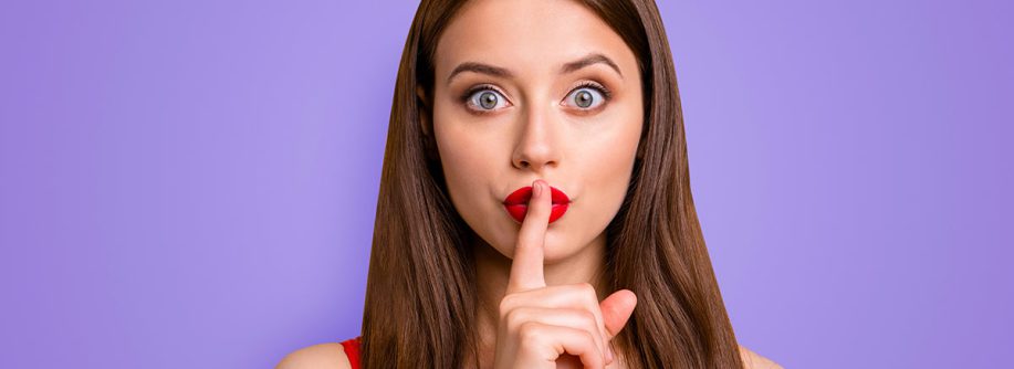 ein junge Frau, die sich den Zeigefinger vor den Mund hält um Verschwiegenheit zu demonstrieren